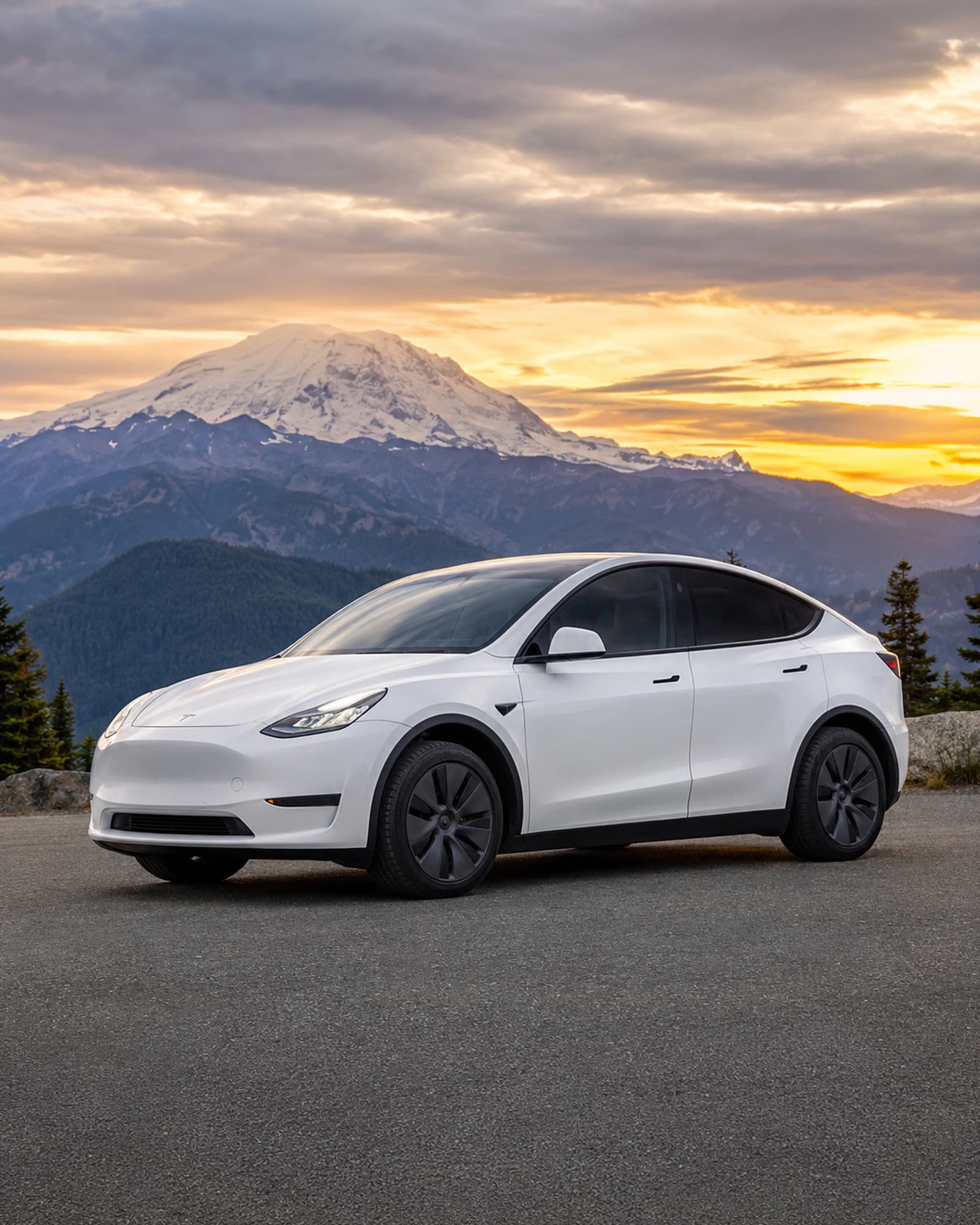 Freedom Rides' flagship Tesla Model Y parked at a viewpoint at sunset, Mount Rainier lit gold behind it.